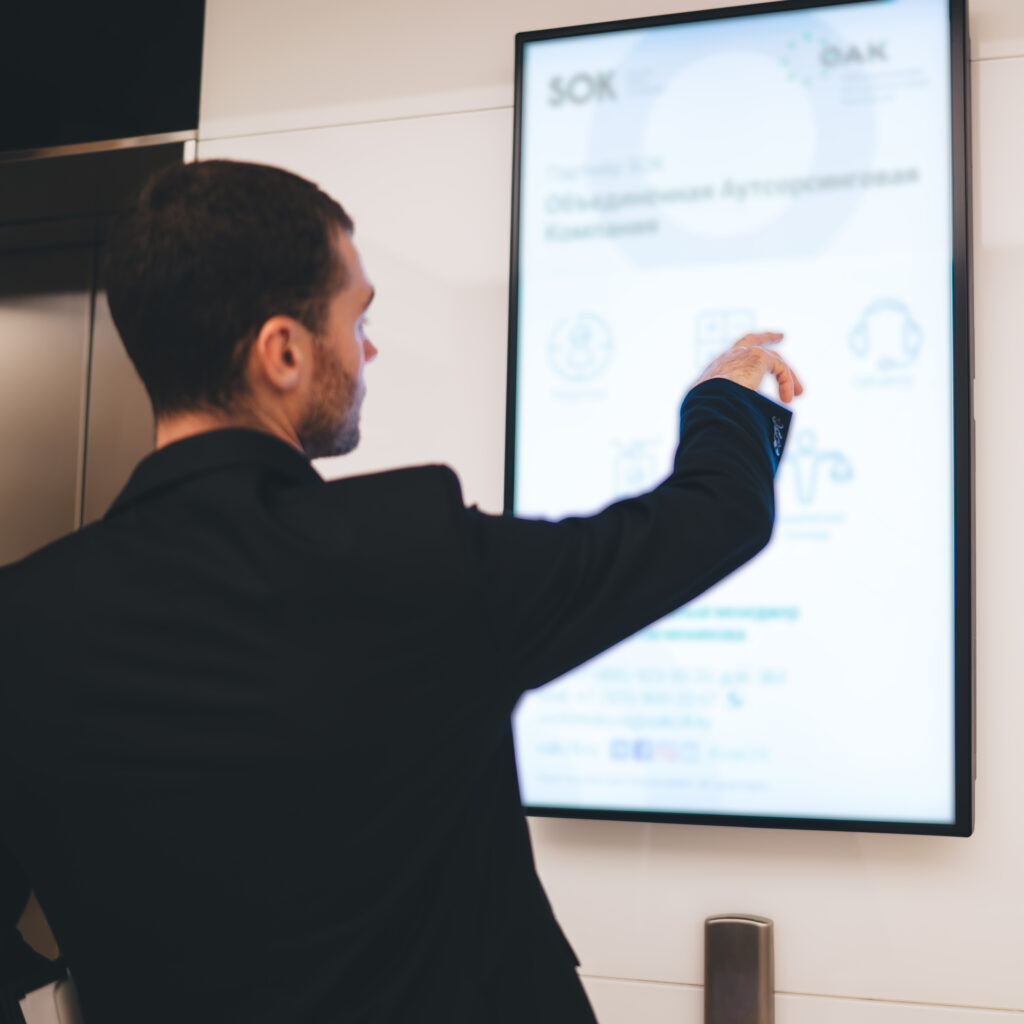 Back view of anonymous businessman standing in office and looking at screen while using hand on tablet and wearing black formal suit